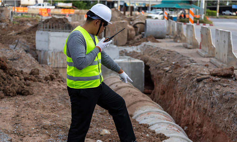 Construction worker inspecting trench with radio