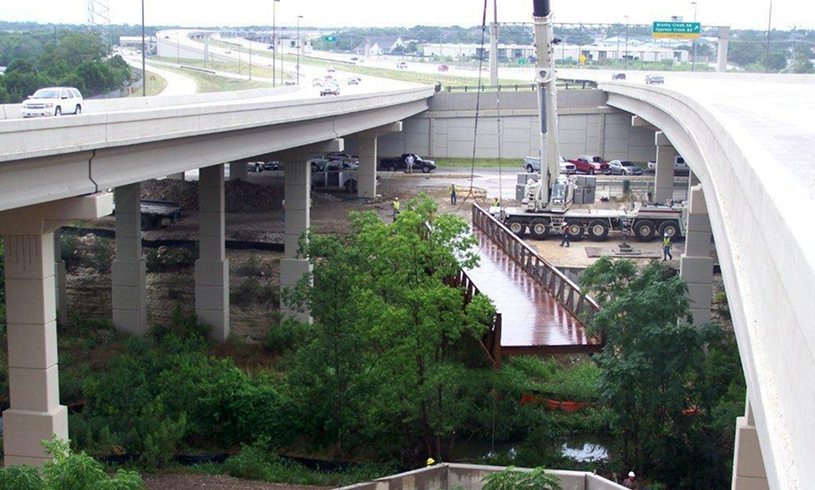 Crane hoisting bridge section under highway
